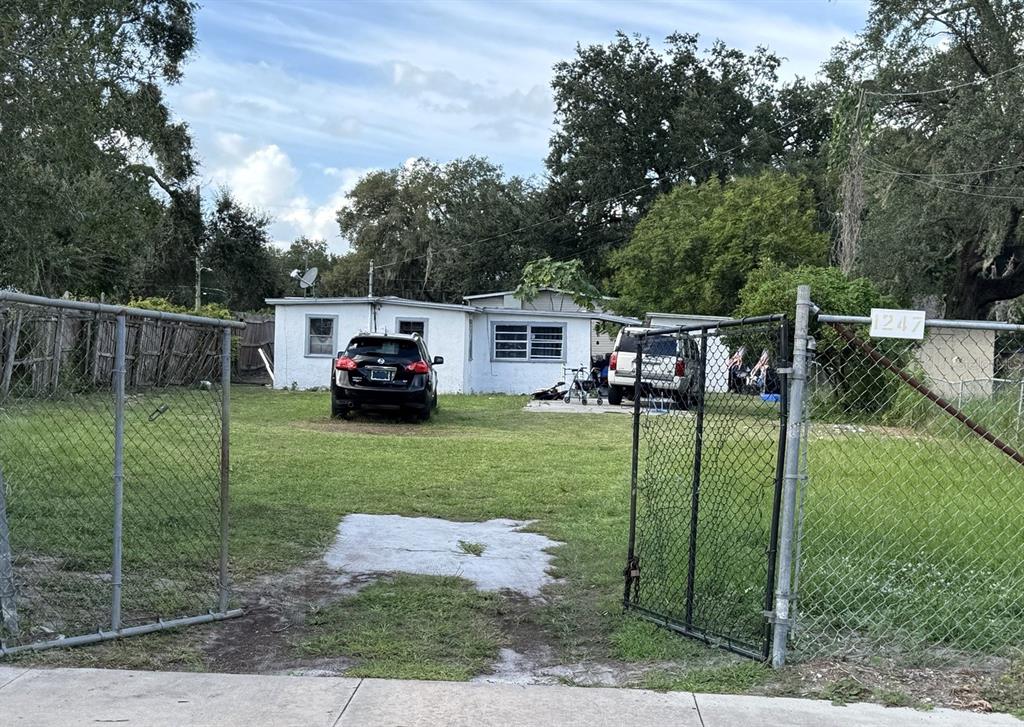 A white single-story house sits behind a chain-link fence with two cars parked in front — 1239 19TH STREET, ORLANDO, FL