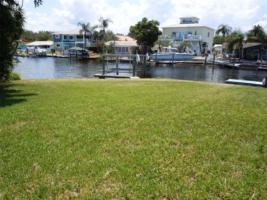 A grassy backyard leads to a canal with boat docks and several waterfront houses — 4850 BONITO DRIVE, NEW PORT RICHEY, FL