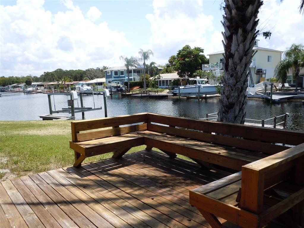 A wooden deck with built-in bench seating overlooks a canal with boat docks and houses — 4850 BONITO DRIVE, NEW PORT RICHEY, FL
