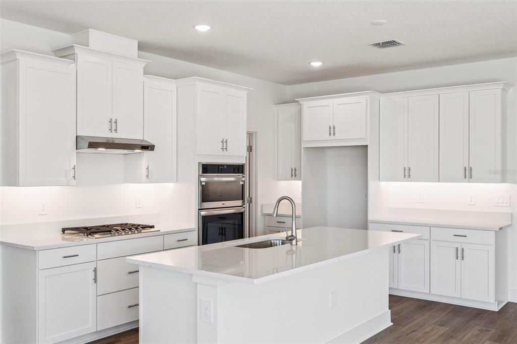 A modern white kitchen features a central island, stainless steel appliances, and quartz countertops — 526 EMERALD GROVE DRIVE, APOPKA, FL