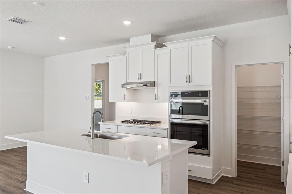 A modern kitchen features white cabinets, a quartz island with a sink, and stainless appliances — 526 EMERALD GROVE DRIVE, APOPKA, FL
