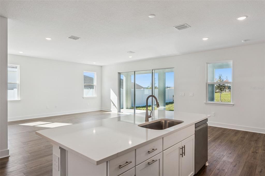 A kitchen island with a sink and white cabinets overlooks an open-concept living area — 526 EMERALD GROVE DRIVE, APOPKA, FL
