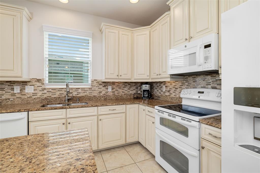 A kitchen features cream cabinets, granite countertops, a tiled backsplash, and white appliances — 7726 111TH TERRACE E, PARRISH, FL