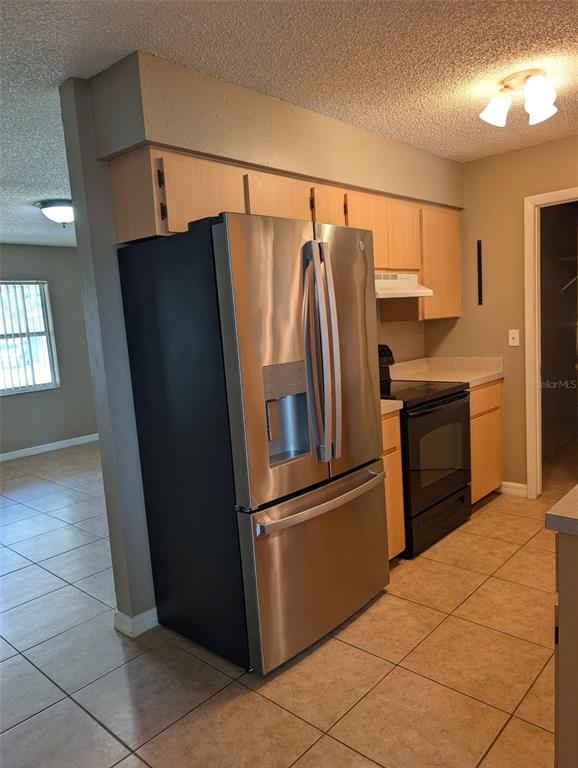 A kitchen features light wood cabinets, stainless steel appliances, and beige tile flooring — 931 CEDAR CIRCLE, TAVARES, FL