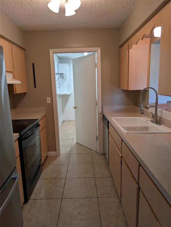 A galley kitchen features light wood cabinets, laminate countertops, a white sink, and tile flooring — 931 CEDAR CIRCLE, TAVARES, FL
