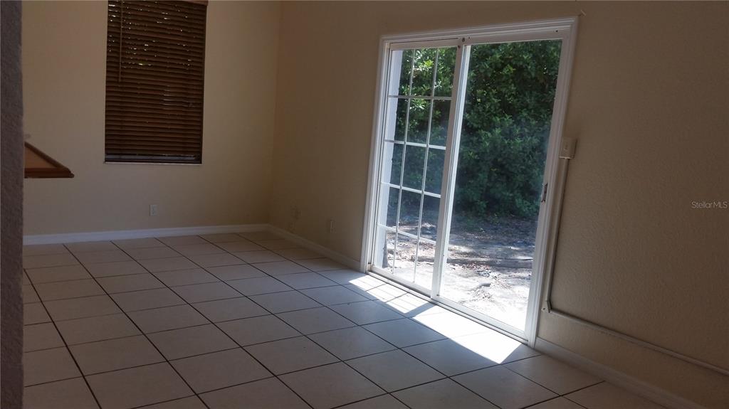 A room with light-colored tile flooring, a window with blinds, and sliding glass patio doors — 931 CEDAR CIRCLE, TAVARES, FL