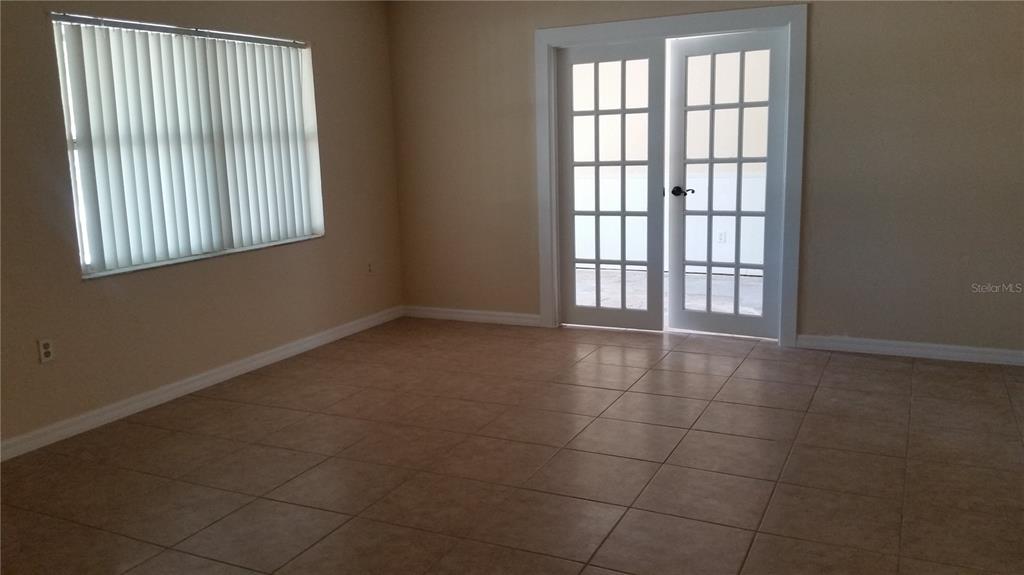 An empty room features beige tile flooring, a window with vertical blinds, and French doors — 931 CEDAR CIRCLE, TAVARES, FL