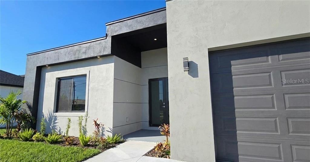 The exterior of a modern house features a gray garage door and a recessed entryway — 1027 KISMET PARKWAY W, CAPE CORAL, FL