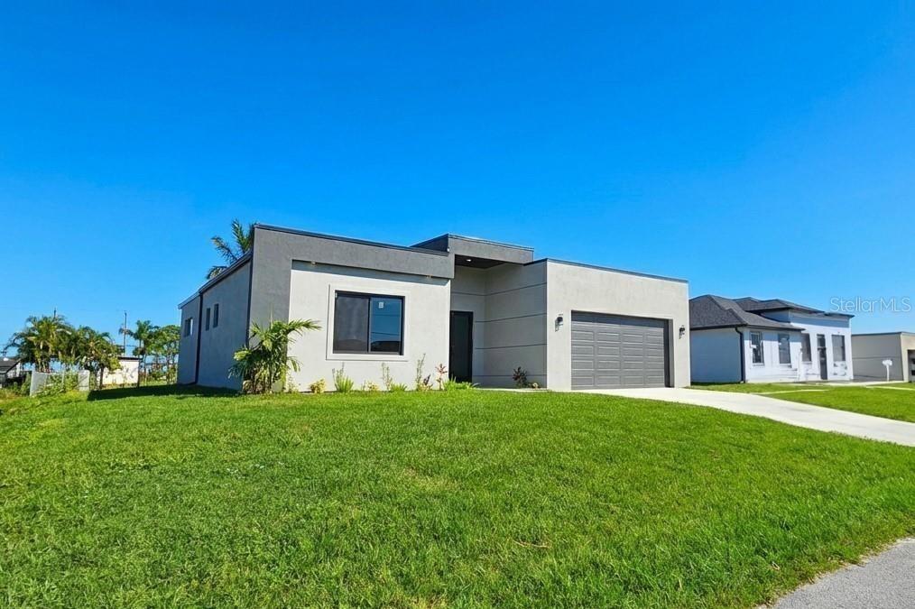 A modern, single-story house with a gray garage and light-colored stucco exterior under clear skies — 1027 KISMET PARKWAY W, CAPE CORAL, FL