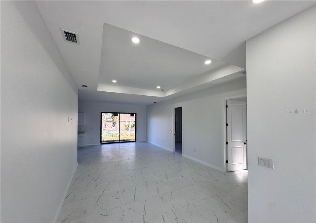 A bright, open-concept living area features white tile flooring, a tray ceiling, and sliding glass doors — 1027 KISMET PARKWAY W, CAPE CORAL, FL