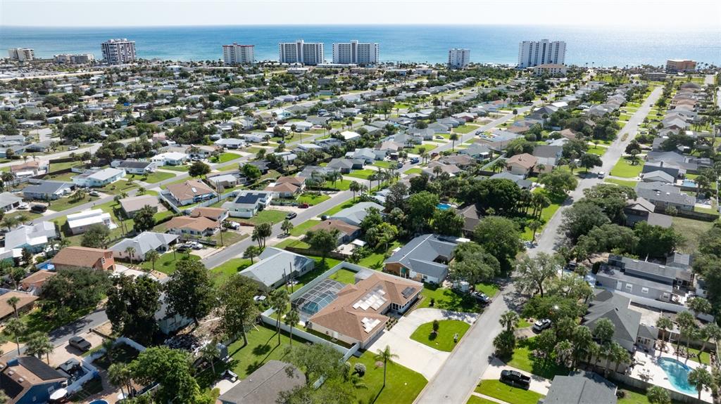 An aerial view shows a residential neighborhood with a beach and high-rise buildings nearby — 33 SANDCASTLE DRIVE, ORMOND BEACH, FL