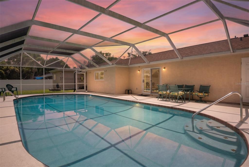 A screened-in swimming pool with a patio and outdoor dining set at sunset — 33 SANDCASTLE DRIVE, ORMOND BEACH, FL