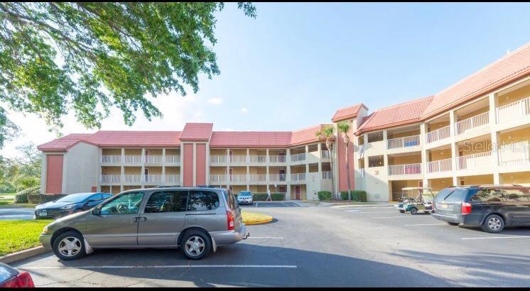 A multi-story apartment building with a red tile roof and a parking lot in front — 6337 PARC CORNICHE DRIVE UNIT 2107, ORLANDO, FL