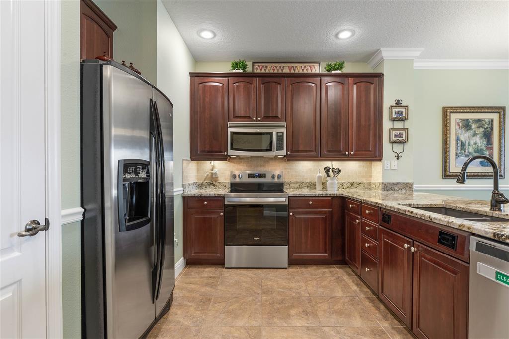 A kitchen features dark wood cabinets, stainless steel appliances, granite countertops, and tile flooring — 75 RIVERVIEW BEND S UNIT 1624, PALM COAST, FL