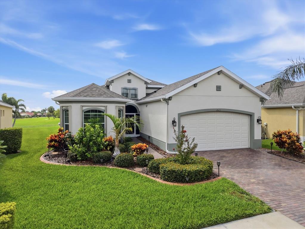 A single-story house with a beige stucco exterior, a two-car garage, and a landscaped yard — 1823 PACIFIC DUNES DRIVE, SUN CITY CENTER, FL