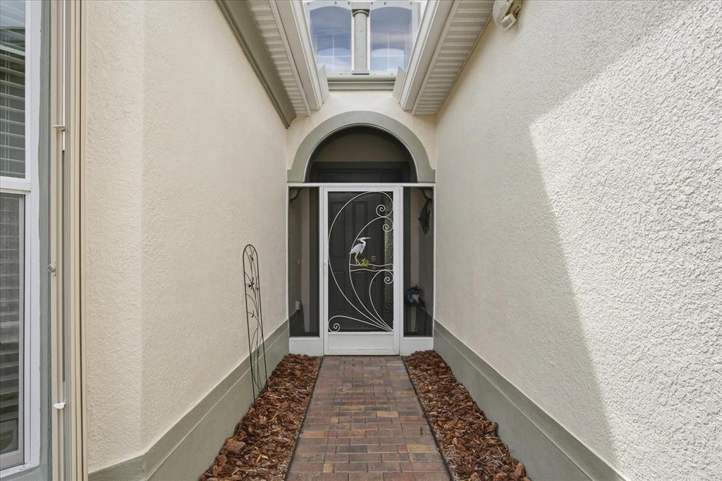 A brick walkway leads to a front door with a decorative screen in a courtyard — 1823 PACIFIC DUNES DRIVE, SUN CITY CENTER, FL