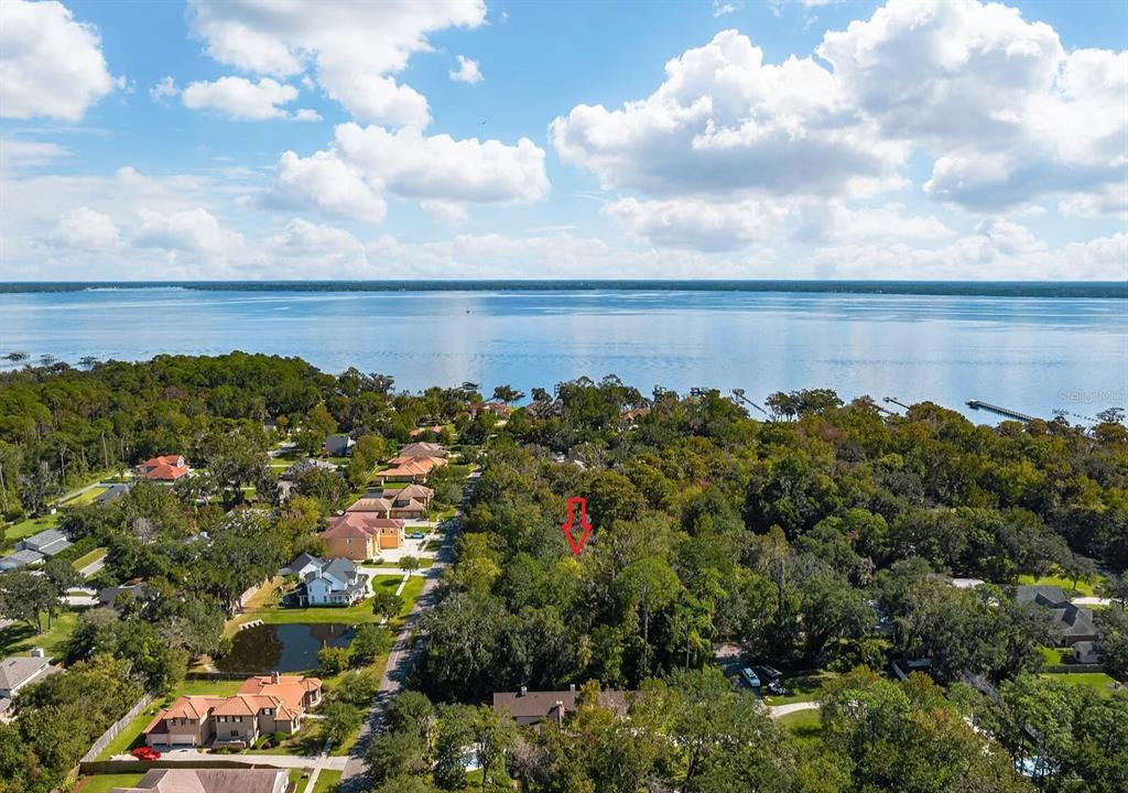 An aerial view shows a wooded residential lot marked by a red arrow near water — RIVERWOOD DRIVE, FLEMING ISLAND, FL
