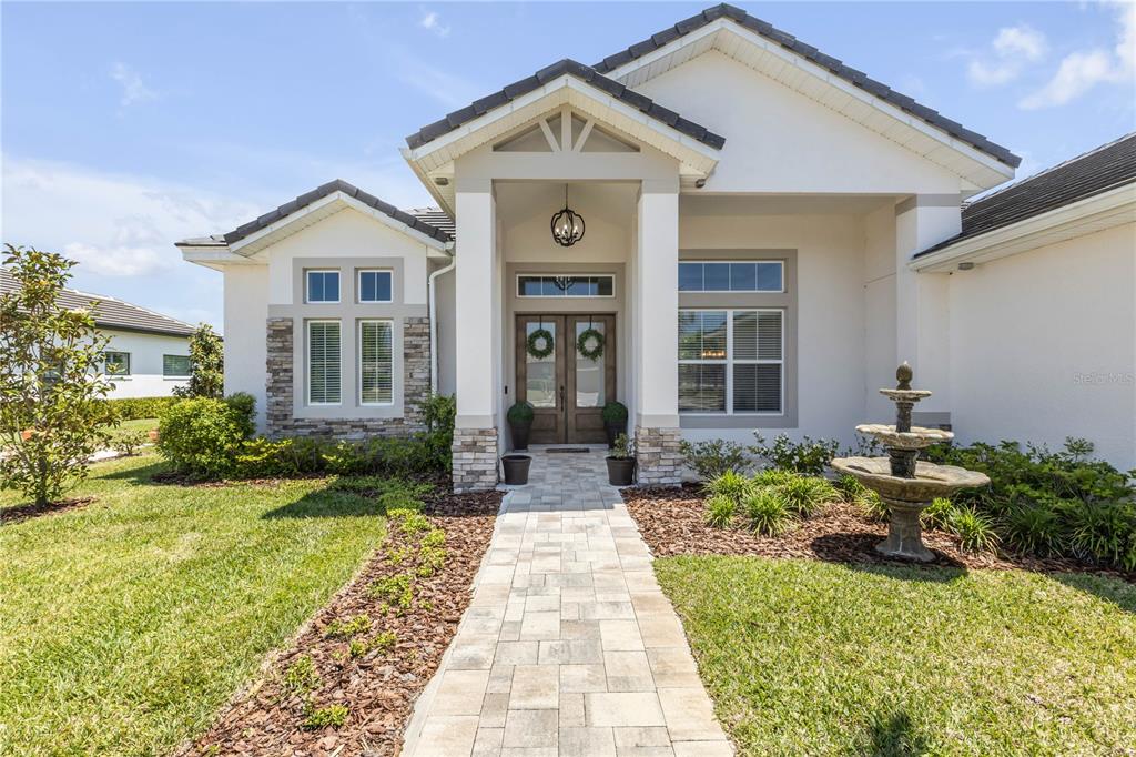 The exterior of a single-story house features a stone-accented entryway, a paved walkway, and a fountain — 3055 ISOLA BELLA BOULEVARD, MOUNT DORA, FL
