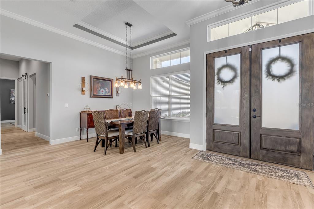 A dining area with a tray ceiling and chandelier sits beside a double front door — 3055 ISOLA BELLA BOULEVARD, MOUNT DORA, FL