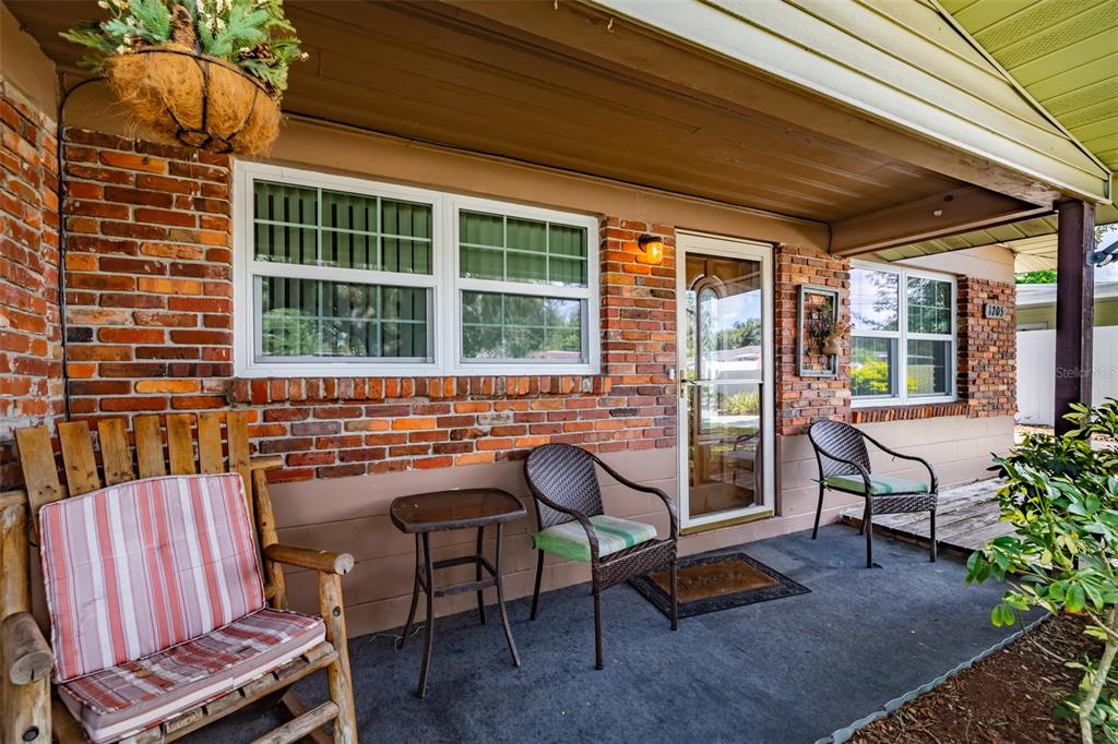 A covered front porch features a brick exterior, a glass storm door, and outdoor seating — 1205 W CAMELLIA DRIVE, BRANDON, FL