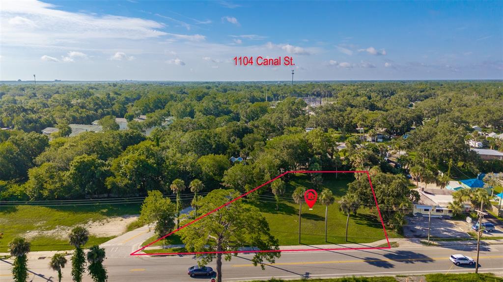An aerial view shows a vacant, grassy lot outlined in red along a paved road — 1104 CANAL STREET, NEW SMYRNA BEACH, FL