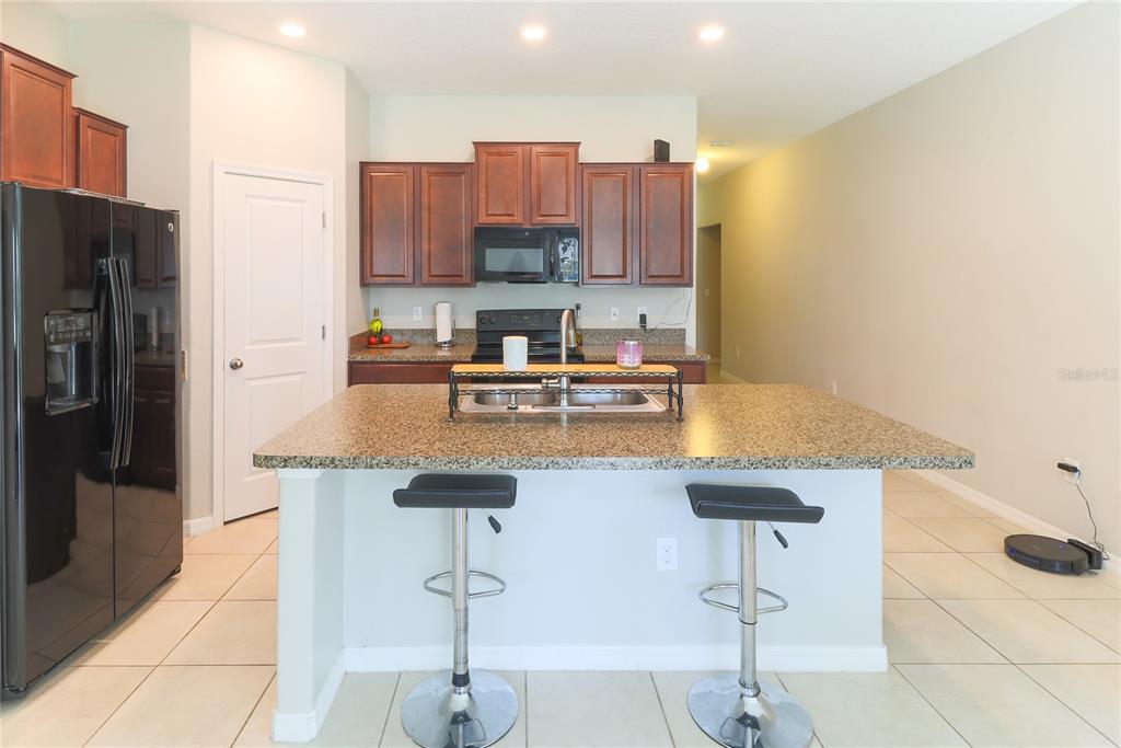 A kitchen features dark wood cabinets, granite countertops, a central island, and two bar stools — 135 CASCADE BEND DRIVE, RUSKIN, FL