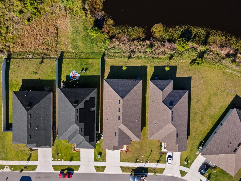 An aerial view shows a row of suburban houses with fenced backyards bordering a pond — 4224 SAGEFIELD DRIVE, HARMONY, FL