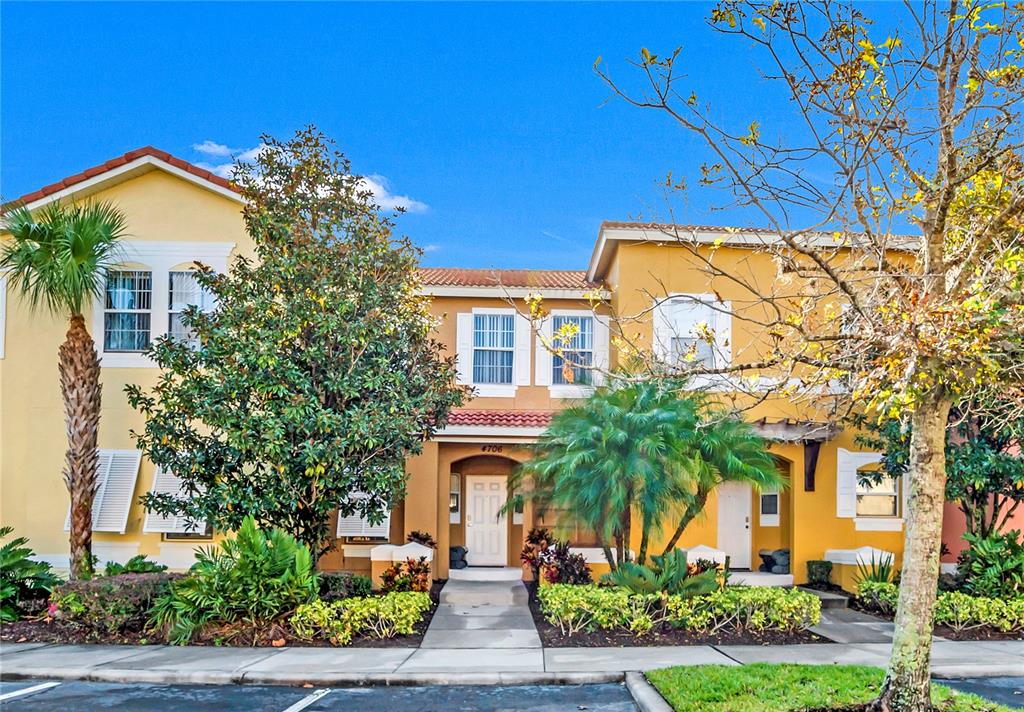 A two-story yellow stucco townhouse features a palm tree, landscaping, and a paved walkway — 4706 VERO BEACH PLACE, KISSIMMEE, FL
