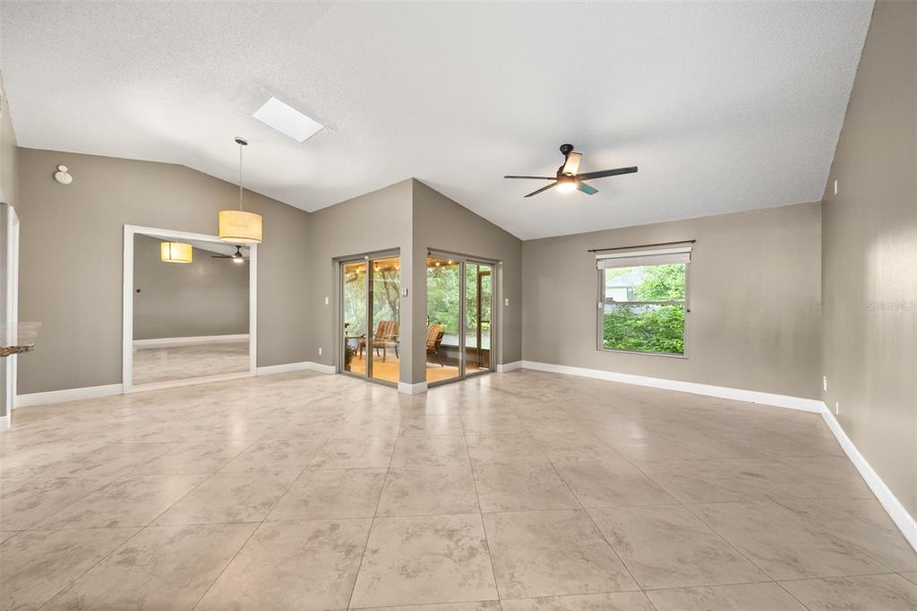 A spacious living room features light-colored tile flooring, a vaulted ceiling, and sliding glass doors — 11813 SCOTTY DRIVE, ORLANDO, FL