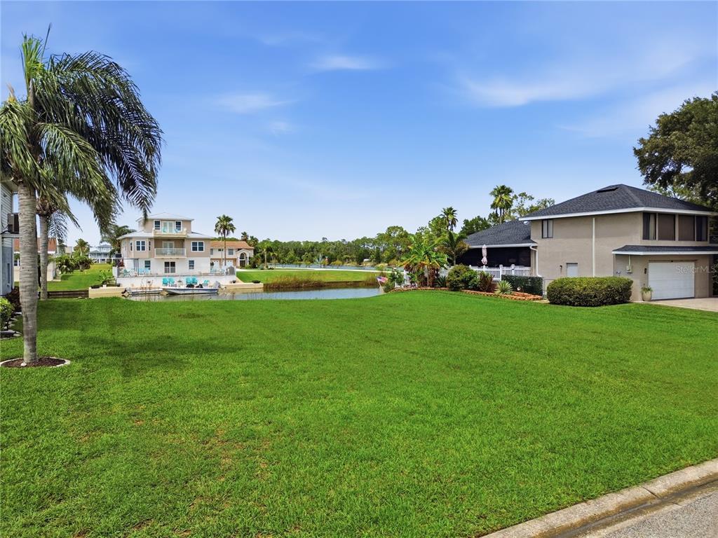 A grassy yard overlooks a canal with houses and palm trees under a blue sky — 4057 JEWFISH DRIVE, HERNANDO BEACH, FL
