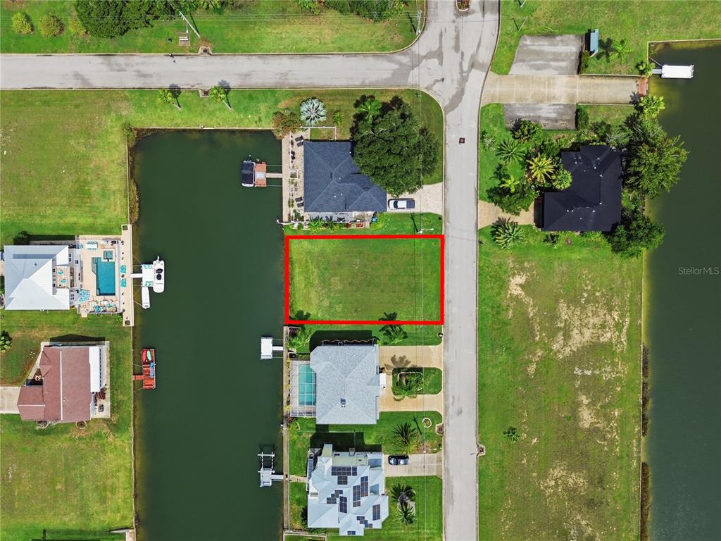 An aerial view shows a vacant rectangular waterfront lot outlined in red between two houses — 4057 JEWFISH DRIVE, HERNANDO BEACH, FL