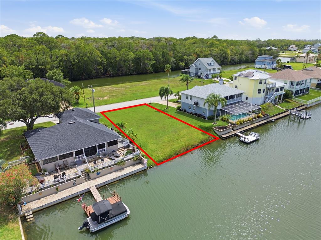 An aerial view shows a vacant waterfront lot outlined in red between two houses — 4057 JEWFISH DRIVE, HERNANDO BEACH, FL