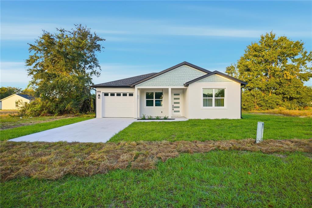A single-story house with a white garage, light-colored siding, and a concrete driveway — 12414 SE 106TH COURT, BELLEVIEW, FL