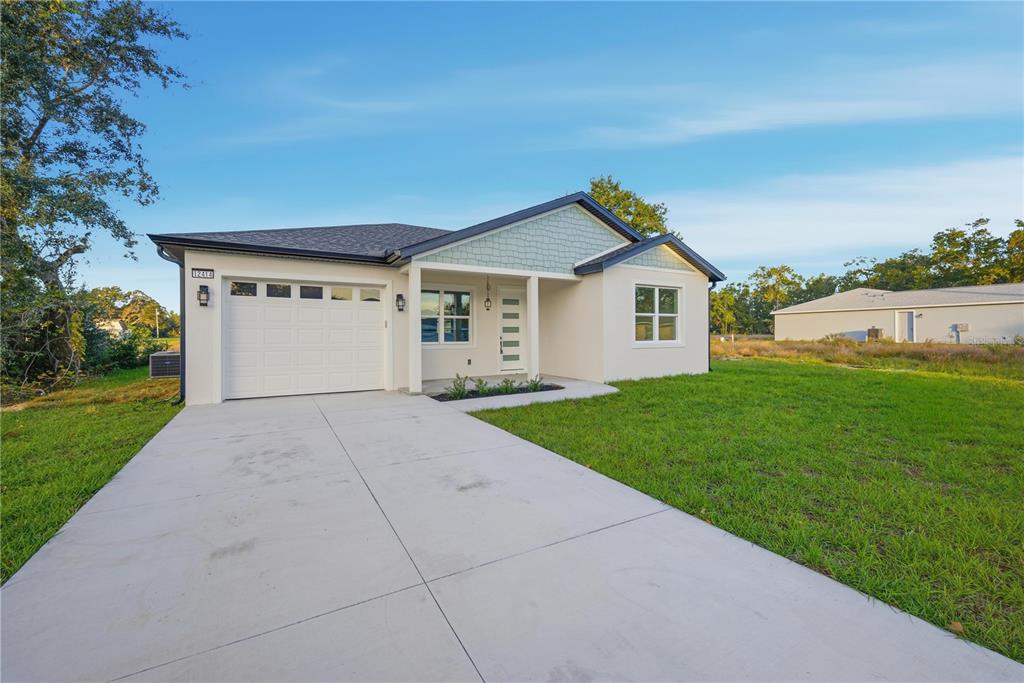 A covered front porch features a white door, a hanging light, and a small garden bed — 12414 SE 106TH COURT, BELLEVIEW, FL