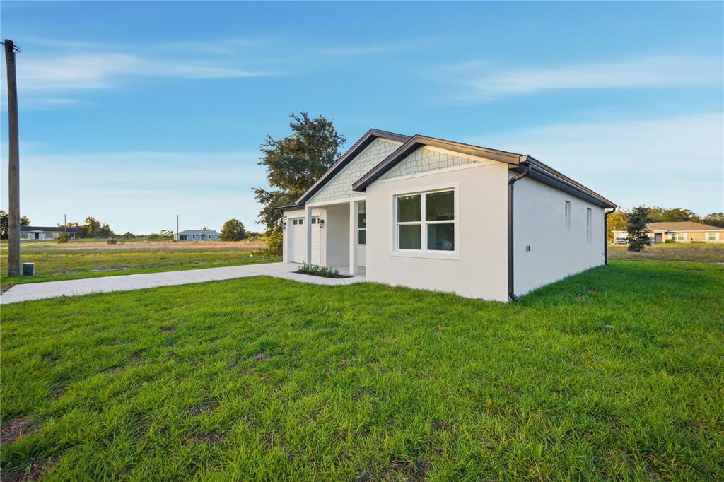 The rear exterior of a single-story house features a screened-in porch and a grassy yard — 12414 SE 106TH COURT, BELLEVIEW, FL