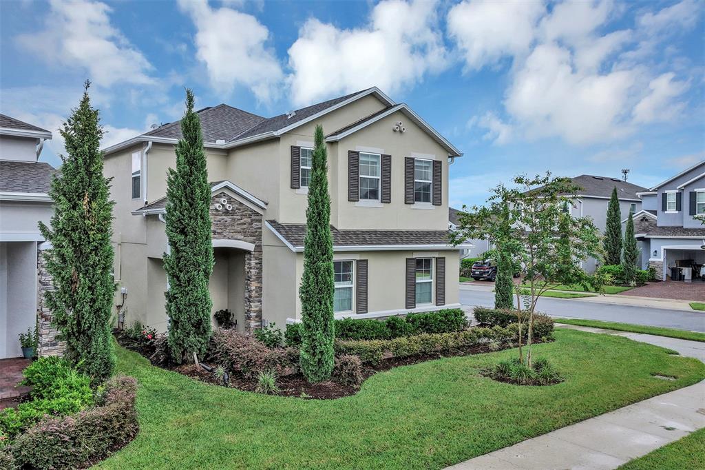 A two-story suburban house with a stone facade, beige siding, and tall, slender evergreen trees — 4504 LATIMER WAY, SANFORD, FL