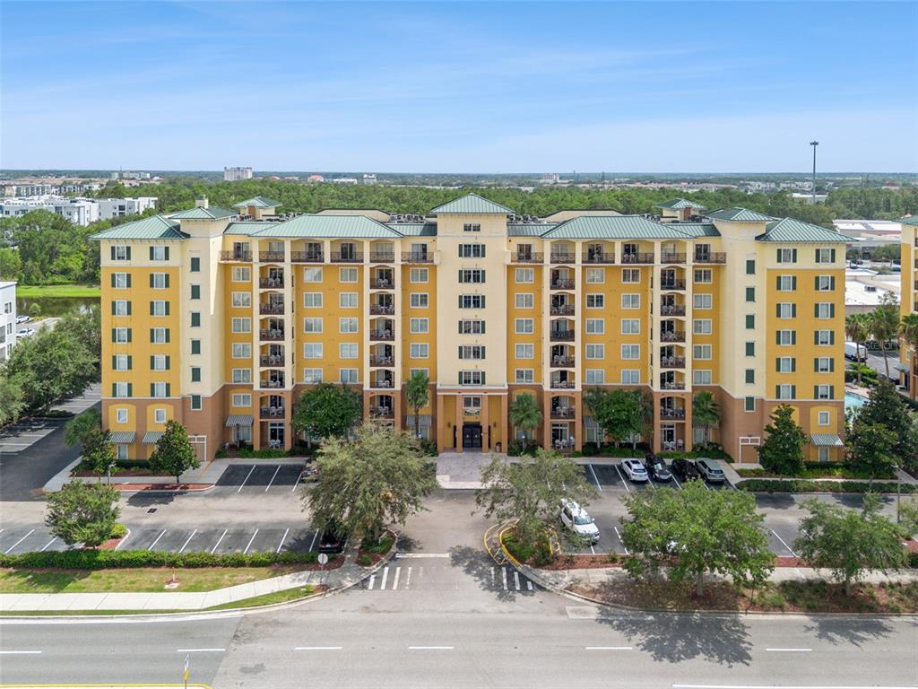 An exterior view of a multi-story yellow apartment building with a green roof and parking — 8100 POINCIANA BOULEVARD UNIT 2703, ORLANDO, FL