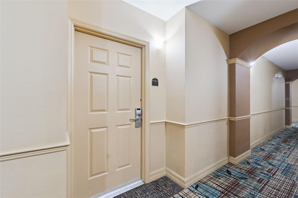 A beige apartment door with a digital lock is located in a carpeted indoor hallway — 8100 POINCIANA BOULEVARD UNIT 2703, ORLANDO, FL