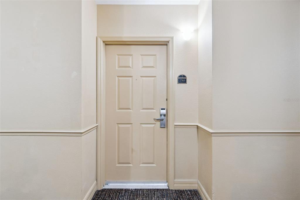 A beige door with a metal handle and room number sign is centered in a hallway — 8100 POINCIANA BOULEVARD UNIT 2703, ORLANDO, FL