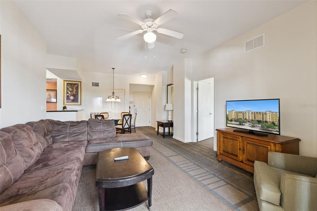 A living room features a brown sectional sofa, a coffee table, and a television console — 8100 POINCIANA BOULEVARD UNIT 2703, ORLANDO, FL