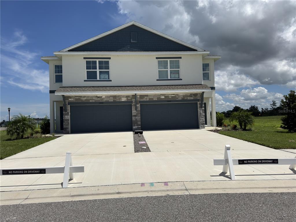 A two-story duplex with two garage doors and a concrete driveway under a cloudy sky — 13609 WOLFPACK ROAD, HUDSON, FL