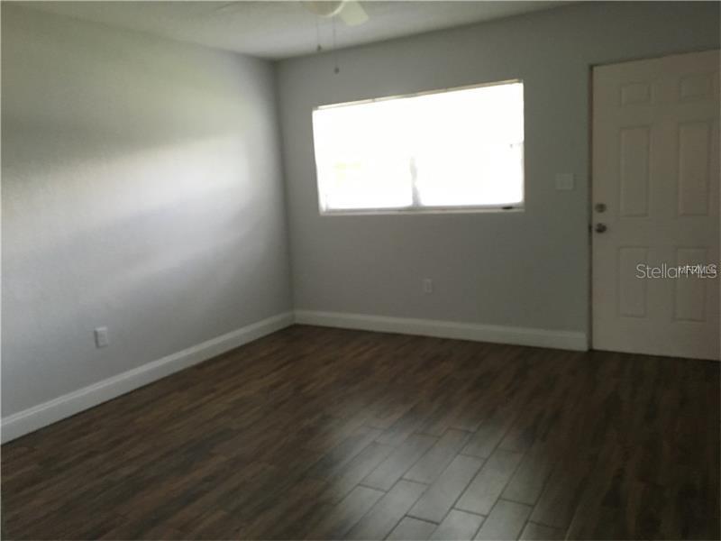 An empty room features light gray walls, dark wood-look flooring, a window, and a white door — 508 VARSITY STREET, WINTER GARDEN, FL