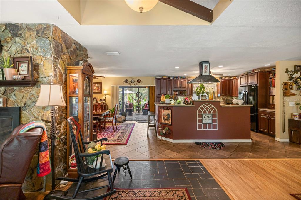 An open-concept living area features a stone fireplace, kitchen with dark cabinets, and tile flooring — 4556 E VIEW TOP LANE, INVERNESS, FL