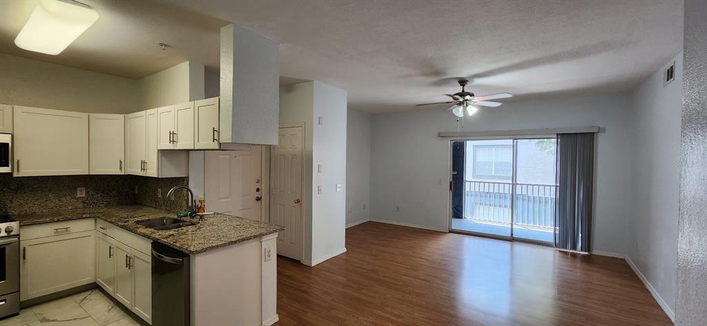 An open-concept kitchen with granite countertops and white cabinets flows into a living area — 13015 SANCTUARY COVE DRIVE UNIT 203, TEMPLE TERRACE, FL