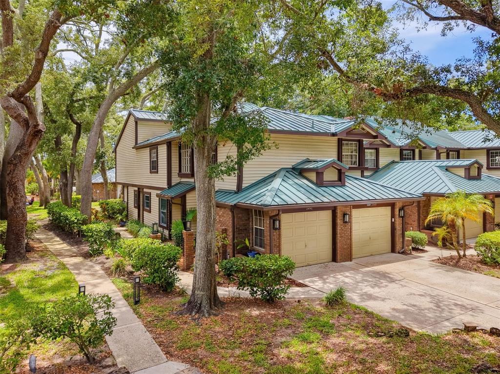 A two-story house with beige siding, a green metal roof, and brick accents — 1491 MAHOGANY LANE UNIT 1491, PALM HARBOR, FL