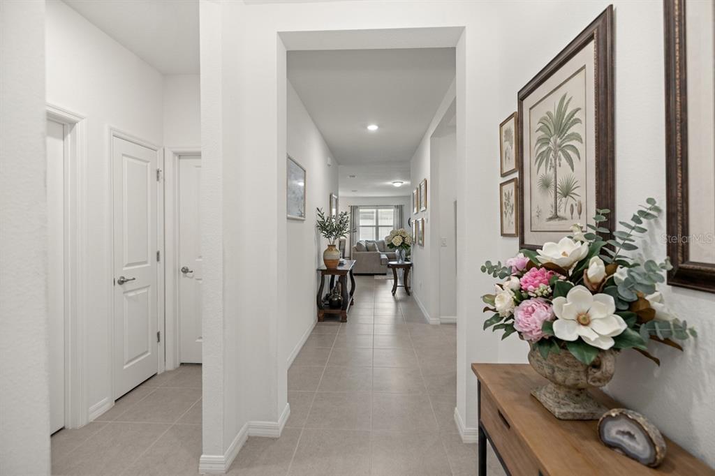 A bright hallway with tile flooring leads toward a living area with a sofa — 6474 SW 89TH LOOP, OCALA, FL