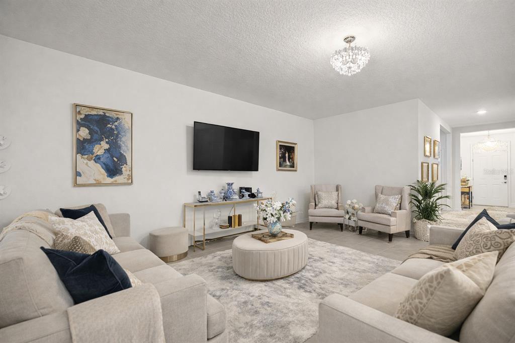 A bright living room features two beige sofas, two armchairs, a central ottoman, and a television — 6474 SW 89TH LOOP, OCALA, FL