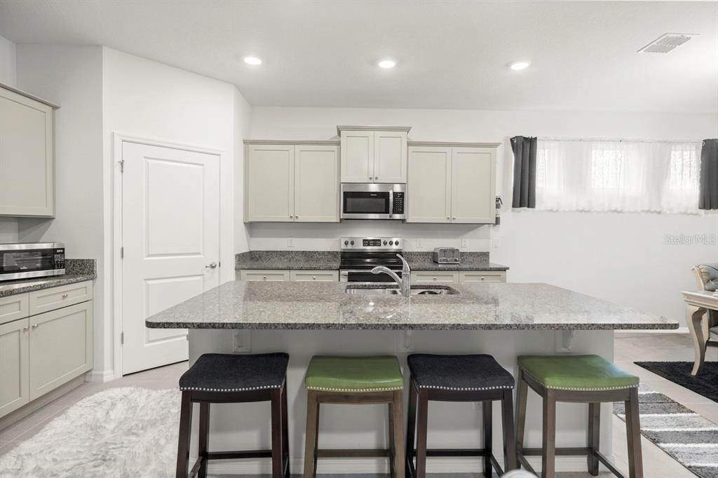 A kitchen features light-colored cabinets, granite countertops, a central island with four stools, and stainless appliances — 6474 SW 89TH LOOP, OCALA, FL