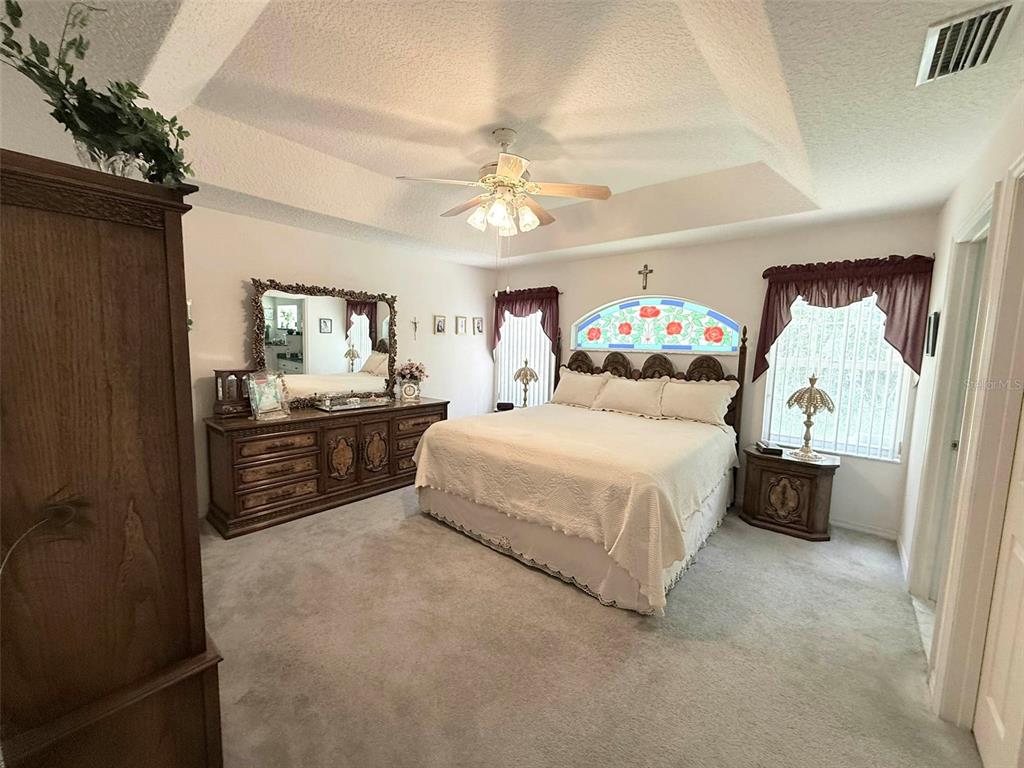 A bedroom features a tray ceiling, a large bed with a stained-glass window, and carpeting — 22 COLORADO DRIVE, PALM COAST, FL