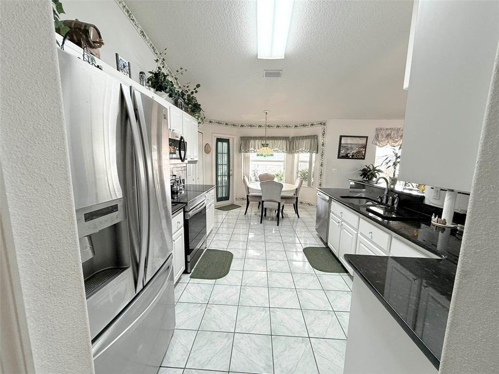 A kitchen with white cabinets, black countertops, and a dining area with a round table — 22 COLORADO DRIVE, PALM COAST, FL